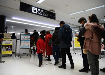 Penumpang yang tiba di salah satu penerbangan terakhir dari Wuhan, China, berjalan melalui stasiun pemeriksaan kesehatan di Bandara Narita di prefektur Chiba, di luar Tokyo, Jumat (24/01). (afp/charly triballeau)