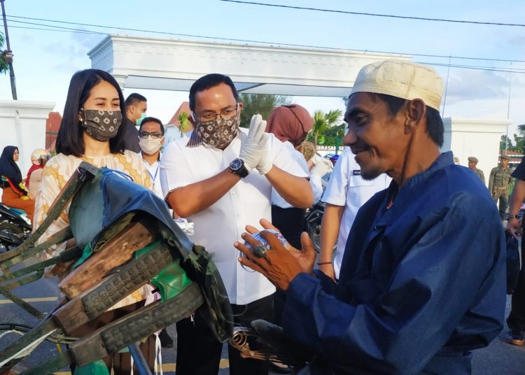 Bupati Muba Dodi Reza Alex dan Ketua TP PKK Muba Thia Yufada membagikan masker kain gratis kepada para pengendara yang lewat di jalan depan rumah dinas Bupati Muba, Senin (06/04). (humas pemkab muba)