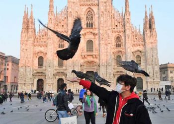 SEORANG pria mengenakan masker sedang bermain dengan merpati di Piazza del Duomo di Milan tengah pada Februari 2020 lalu. Karantina di Italia diberlakukan setelah pemerintah khawatir virus corona akan menyebar di Roma, akibatnya pariwisata di Italia mengalami penurunan. (Miguel Medina/AFP/Getty Images)