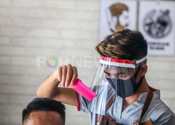 Tukang cukur melayani pelanggan sambil menggunakan face shield dan masker. (matakamera/fornews.co/mushaful imam)
