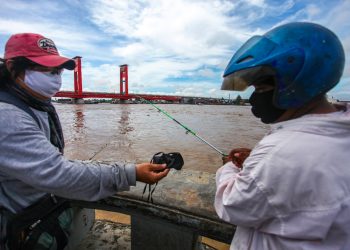 Ketua PFI Palembang Abriansyah Liberto saat membagikan masker kepada warga yang sedang memancing di kawasan BKB, Palembang, Selasa (19/05). (fornews.co/pfi palembang)