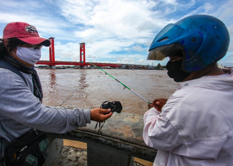 Ketua PFI Palembang Abriansyah Liberto saat membagikan masker kepada warga yang sedang memancing di kawasan BKB, Palembang, Selasa (19/05). (fornews.co/pfi palembang)