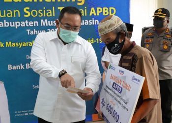 Bupati Muba Dodi Reza Alex menunjukkan buku tabungan yang saldonya berisikan Bantuan Sosial Tunai (BST) APBD Kabupaten Musi Banyuasin Tahun 2020 kepada salah seorang keluarga penerima manfaat (KPM) di Kantor BRI Cabang Sekayu, Rabu (20/05). (fornews.co/humas pemkab muba)