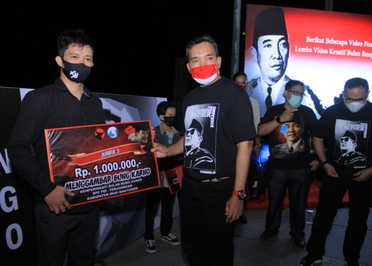 Ketua DPC PDI Perjuangan Kabupaten Muba Beni Hernedi menyerahkan hadiah ke pemenang ketiga lomba menggambar sketsa Bung Karno pada malam puncak Bulan Bung Karno di waterfront Sekayu, Senin (27/07) malam. (fornews.co/humas pemkab muba)