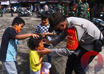 Petugas kepolisian memakaikan masker kepada anak di Pasar KM 5. Petugas kepolisian dan pekerja publik lainnya dijadwalkan vaksinasi Covid-19 mulai 17 Februari 2021. (matakamera/fornews.co/mushaful imam)