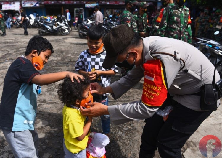 Petugas kepolisian memakaikan masker kepada anak di Pasar KM 5. Petugas kepolisian dan pekerja publik lainnya dijadwalkan vaksinasi Covid-19 mulai 17 Februari 2021. (matakamera/fornews.co/mushaful imam)