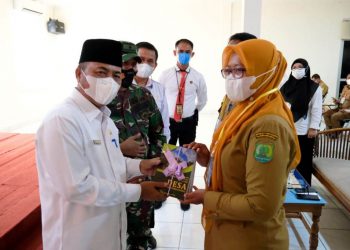 Sekda Muba Apriyadi menyerahkan buku tentang pemerintahan desa kepada salah satu peserta Bimtek Kepala Desa dan Perangkat Desa di Muba, Senin (5/4/2021). (fornews.co/humas pemkab muba)