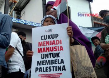 SEORANG ibu dan anak membentang poster dan bendera kecil turut dalam aksi damai dukung Palestina di Titik Nol Kilometer Kota Yogyakarta pada Jum’at (21/5/2021). (foto fornews.co/adam)