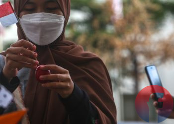Pedagang sedang memasang bendera di telok abang yang akan dipasang di mainan kapal kapalan, sementara pembeli sedang mengabadikan mengunakan smartphone. Dengan smartphone si pembeli dapat berbagi cerita kebaikan dan informasi melalui media sosial kepada masyarakat lainnya, di Jalan Merdeka, Senin (16/8/2021). (fornews.co/mushaful imam)