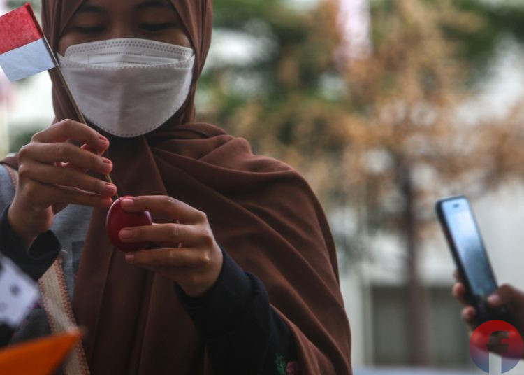 Pedagang sedang memasang bendera di telok abang yang akan dipasang di mainan kapal kapalan, sementara pembeli sedang mengabadikan mengunakan smartphone. Dengan smartphone si pembeli dapat berbagi cerita kebaikan dan informasi melalui media sosial kepada masyarakat lainnya, di Jalan Merdeka, Senin (16/8/2021). (fornews.co/mushaful imam)