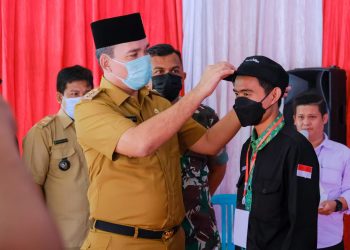 Plt Bupati Muba, Beni Hernedi mengalungkan tanda peserta dan pemasangan topi kepada panitia IMMUBA Mengajar di Balai Desa Keramat Jaya Kecamatan Sungai Keruh, Selasa (15/2/2022). (fornews.co/humas pemkab muba)