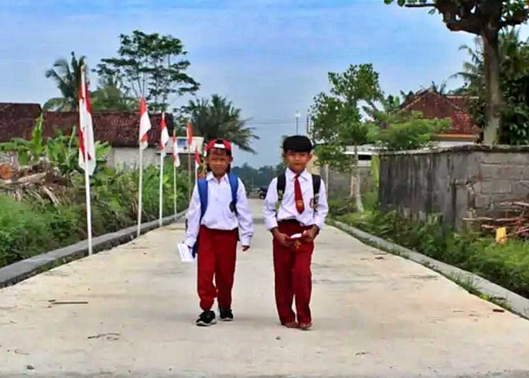 DUA pelajar sekolah dasar (SD) berangkat sekolah melewati jalan yang sudah selesai dibangun TMMD Reguler ke-124 Kodim 0732/Sleman. (foto fornews.co/tni)