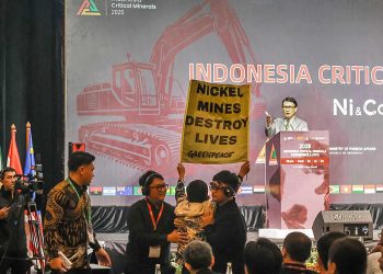 SEORANG aktivis Greenpeace membentangkan spanduk bertuliskan, "Berapa Biaya Sebenarnya dari Nikel Anda?" dalam bahasa Inggris dan membentangkan spanduk lain dengan pesan bahwa tambang Nikel telah menghancurkan kehidupan. (foto fornews.co/greenpeace indonesia)