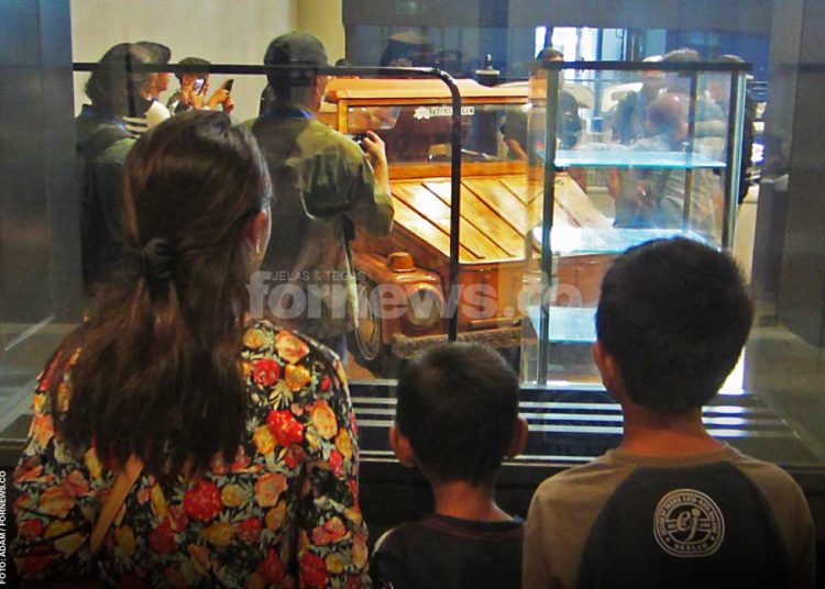 INGIN masuk tapi ragu, dua anak bersama ibunya hanya melihat dari balik kaca, Jum'at sore (11/7/2025). Mereka tampak serius mengamati mobil Volkswagen berbody kayu yang dipamerkan JVWF 2025 di Gelanggang UGM yang berlangsung tanggal 10-13 Juli 2025. (foto fornews.co/adam)